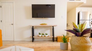A modern kitchen with a flat-screen TV mounted above a wooden shelf, a refrigerator, and potted plants. - ༄The Agave Ranch༄ FREE Pool Heating & Arcade Room! (Phoenix)