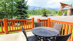 Un espace extérieur aménagé avec une table ronde et des chaises, une clôture en bois, et une vue sur un parking et des montagnes en arrière-plan.