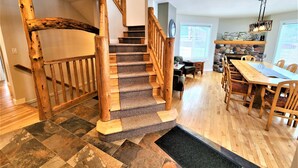 Un escalier en bois avec des marches recouvertes de moquette, un coin repas avec une longue table et des chaises en bois, et une cheminée en pierre.