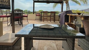 An outdoor patio area with a covered seating area, a table with a glass top, wicker furniture, and a view of the landscape.