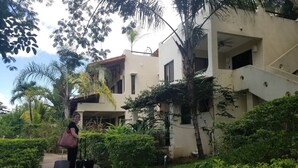 Une personne, avec des bagages, se trouve sur un chemin menant à un bâtiment à la façade blanche et doté de nombreuses fenêtres.