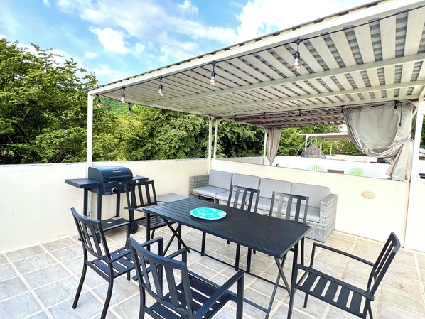 Un patio al aire libre con una mesa, sillas, una parrilla y una zona de estar techada.
