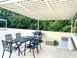 An outdoor patio with a table and chairs, a grill, and a cushioned seating area.