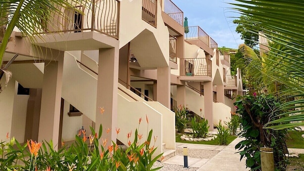 A resort with multiple-story buildings, outdoor staircases, and lush greenery including palm trees and flowering plants. - Parakeet Paradise 2nd floor Condo with Rooftop (Playas Del Coco)