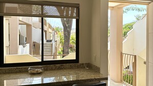 A kitchen with a granite countertop, three bar stools, a window with a view of a balcony and trees, and a door leading to an outdoor area. - Parakeet Paradise 2nd floor Condo with Rooftop (Playas Del Coco)