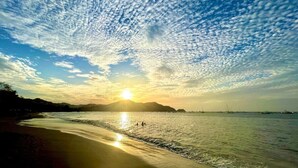 A beach with a clear sky and the sun setting or rising over the water. - Parakeet Paradise 2nd floor Condo with Rooftop (Playas Del Coco)