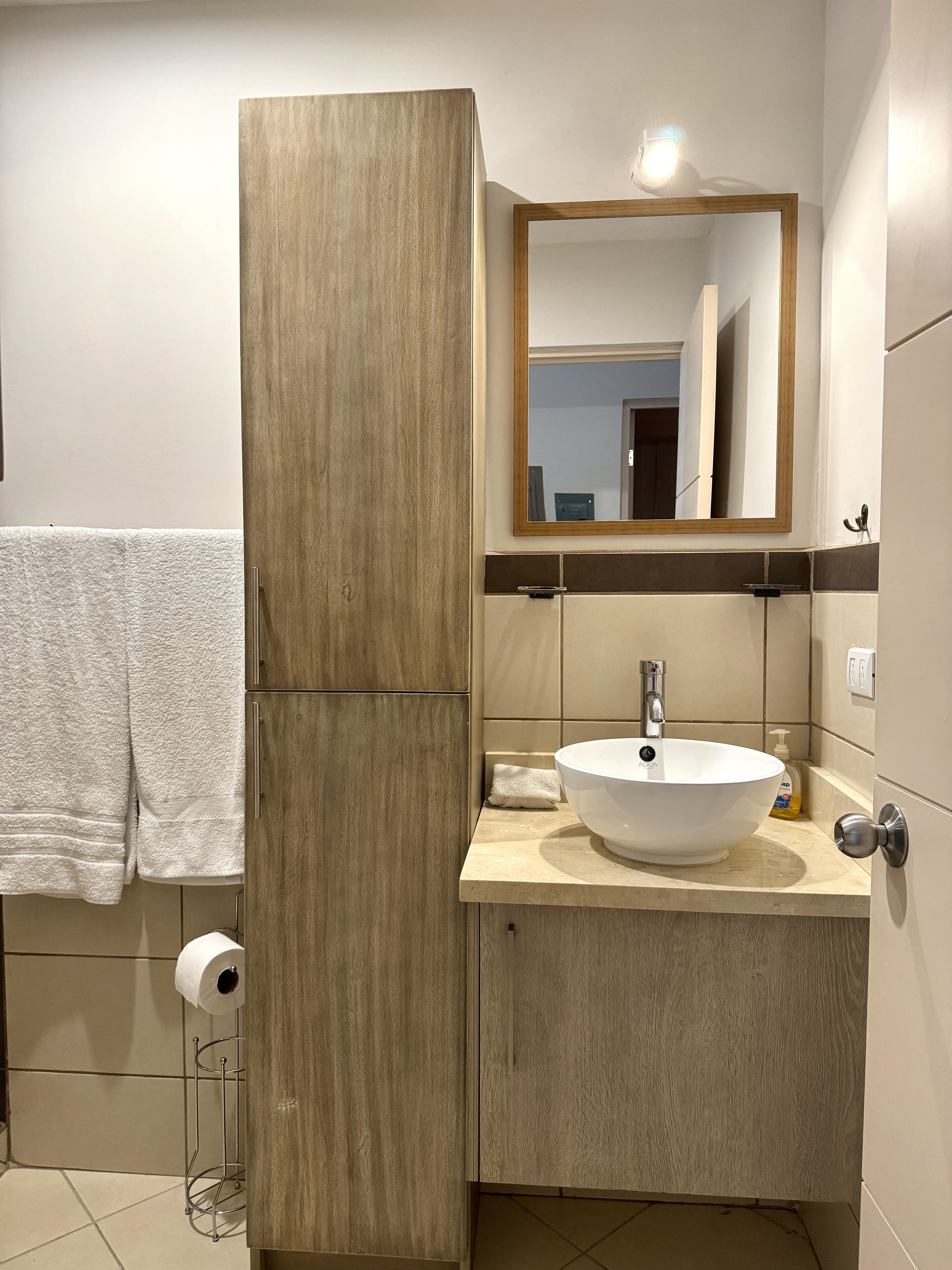 A bathroom with a wooden vanity, a white sink, a mirror, and a towel rack.