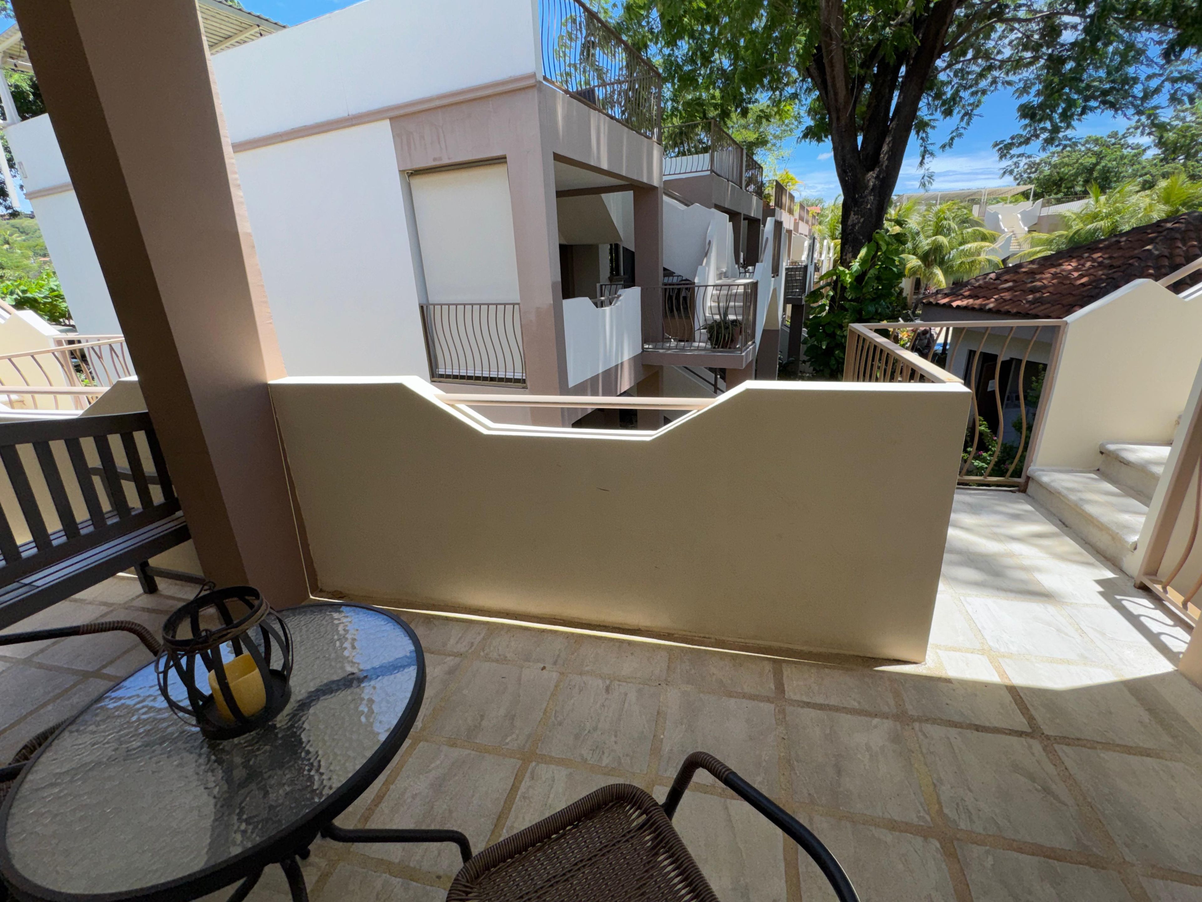 A terrace with a table and chairs, a white wall, and a view of a building with balconies.