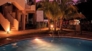 Un edificio moderno con piscina, rodeado de palmeras y un cielo morado.