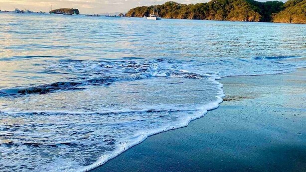 A beach with waves and a distant island. - EndlessSummer Beach Escape (Playas Del Coco)