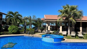 A swimming pool with a blue mosaic border, surrounded by palm trees and lounge chairs.