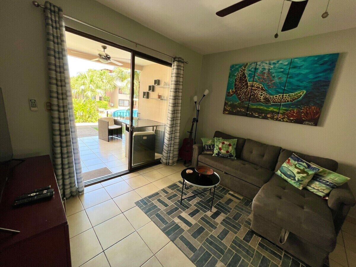 A living room with a sofa, a coffee table, and a painting of a turtle. There is a sliding glass door leading to an outdoor area with a table and chairs.