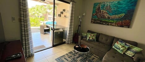 A living room with a sofa, a coffee table, and a painting of a turtle. There is a sliding glass door leading to an outdoor area with a table and chairs.