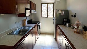 A kitchen with a central island, a built-in oven, a refrigerator, and a window with patterned glass. - Sea Bottom Ground Condo (Playas Del Coco)