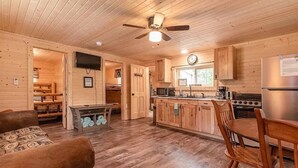 Interior acogedor de una cabaña con piso de madera, un comedor con mesa y sillas, una cocina con electrodomésticos modernos y un ventilador de techo.