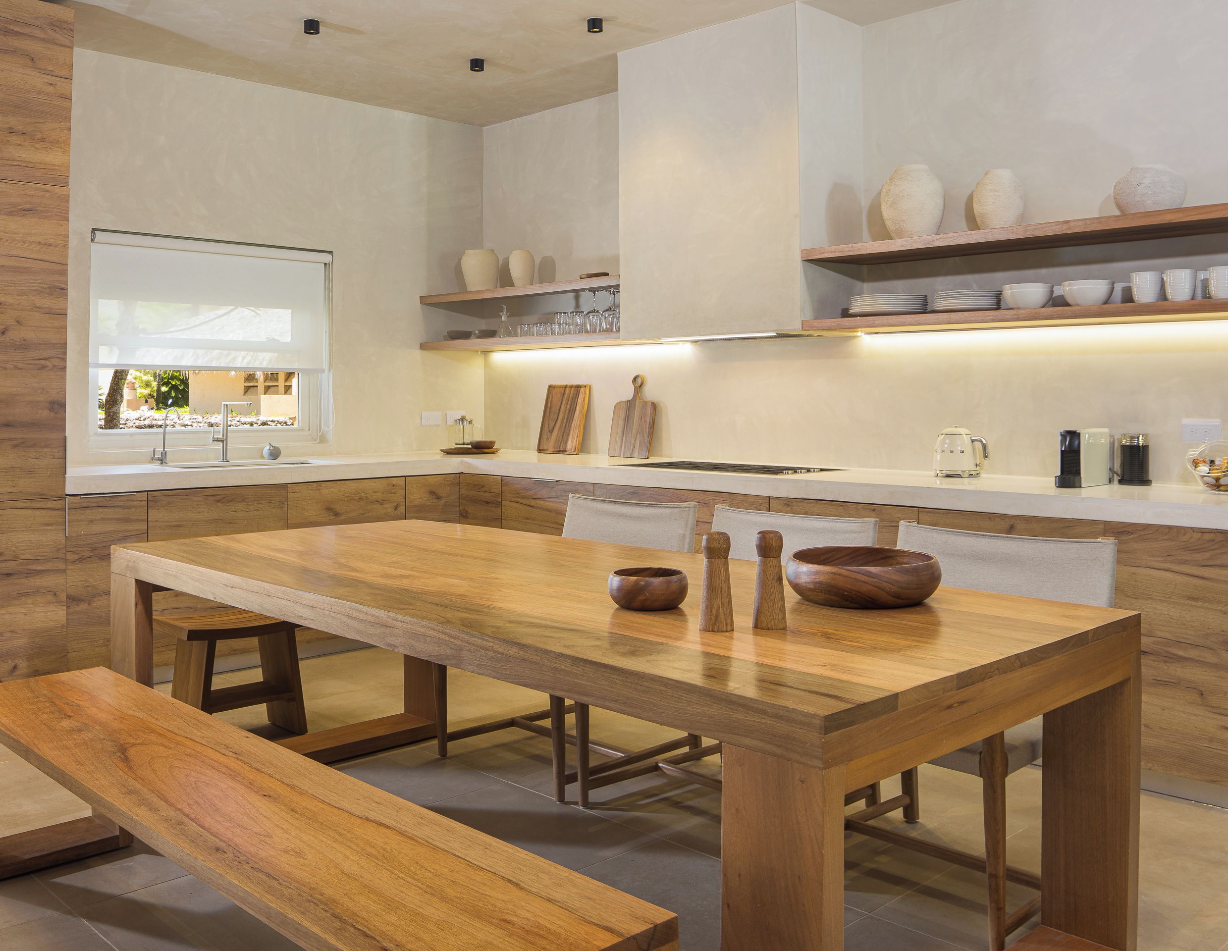 A modern kitchen with a wooden dining table, benches, and a view of the outdoors.