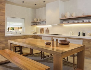 A modern kitchen with a wooden dining table, benches, and a view of the outdoors.