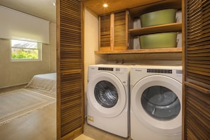 A laundry room with two front-loading washers, wooden cabinets above, and a window with a view of greenery.