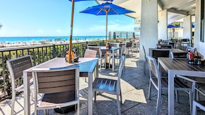 Un patio al aire libre con mesas y sillas, sombrillas azules y vista a la playa.