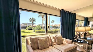 Una sala de estar con un sofá a rayas, una mesa de centro con decoración de estrellas de mar y vistas a un césped verde y palmeras.