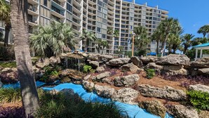 Un resort con piscina, palmeras y un edificio grande con balcones.