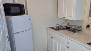 A compact kitchen with white cabinets, a white refrigerator, a microwave, a sink, and a black mat on the floor. - TheVacaVacationHomes (Lauderdale Lakes)