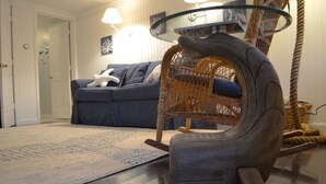 A living room with a blue sofa, a wicker rocking chair, a glass coffee table, and a patterned rug. - Cozy Nautical Getaway in Cape Neddick (Ogunquit)