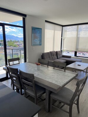 A modern living room with a dining area, large windows, and a city view.