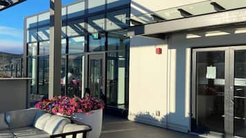 Un bâtiment moderne doté de grandes fenêtres en verre, d’une terrasse en bois et d’un espace extérieur aménagé pour s’asseoir.