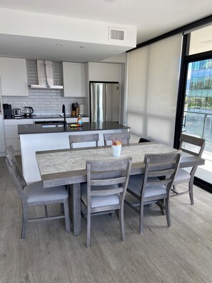 A modern kitchen with a central island, stainless steel appliances, and a dining area with wooden chairs and a marble table.