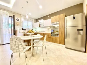 Une cuisine moderne dotée d’un îlot central, de meubles en bois, d’un réfrigérateur en acier inoxydable et d’un coin repas avec des chaises à structure métallique.