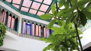 A room with a high ceiling, arched windows, and hanging plants. - Hotel Riad Dar El Qdima (Essaouira)