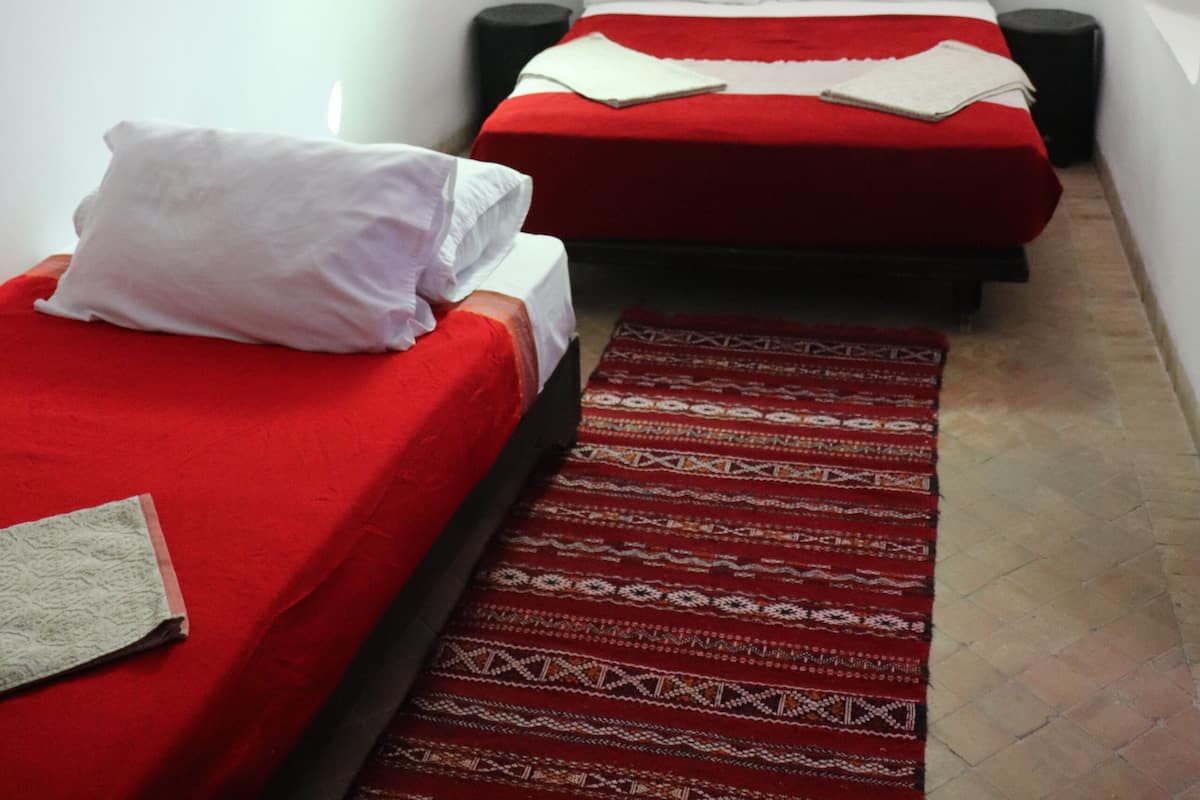 A narrow room with two beds, one on each side, and a small window at the end.