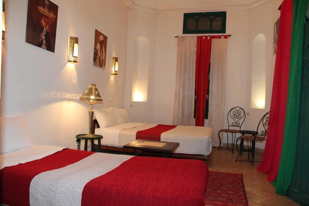Une chambre d’hôtel avec deux lits, une table, des chaises et des appliques murales décoratives.