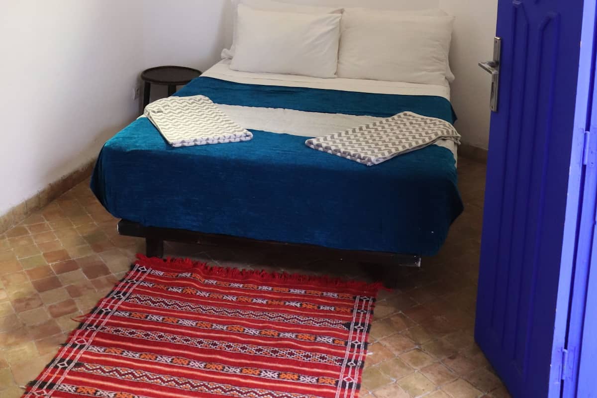 A small, narrow room with a bed, a window, and a door.