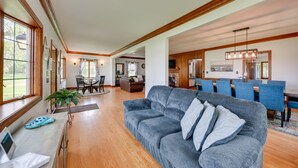A spacious living room with a grey sofa, wooden flooring, and a dining area with blue chairs. - Pistakee Lake Estate w/ Boat Dock & Hot Tub! (Johnsburg)