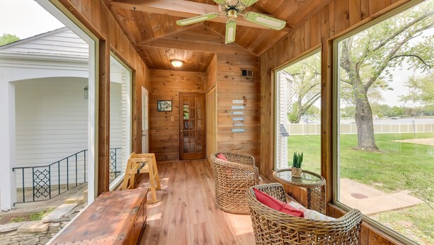 A wooden interior with a ceiling fan, wicker chairs, a wooden table, and large windows offering a view of the outdoors. - Pistakee Lake Estate w/ Boat Dock & Hot Tub! (Johnsburg)