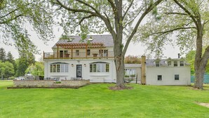 A two-story house with a balcony, a large tree in the front yard, and a well-maintained lawn. - Pistakee Lake Estate w/ Boat Dock & Hot Tub! (Johnsburg)