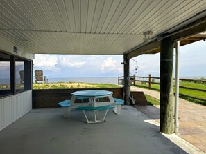A covered outdoor seating area with a table and benches, overlooking a beach and the sea. - Secluded Beach home with amazing views.  (Milford)