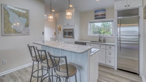 A modern kitchen with a central island, bar stools, pendant lights, a refrigerator, and a window with a view. - Secluded Beach home with amazing views.  (Milford)