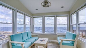 A sunroom with large windows overlooking the ocean, a white ceiling fan, and a light-colored wooden floor. - Secluded Beach home with amazing views.  (Milford)