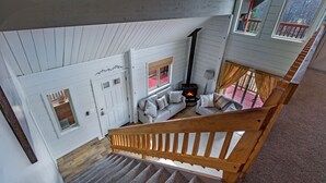 Una scala conduce a una camera da letto soppalcata con camino, una porta bianca e vista sull'esterno.