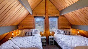 Una camera da letto mansardata accogliente con due letti, pareti in legno e vista sull'esterno.