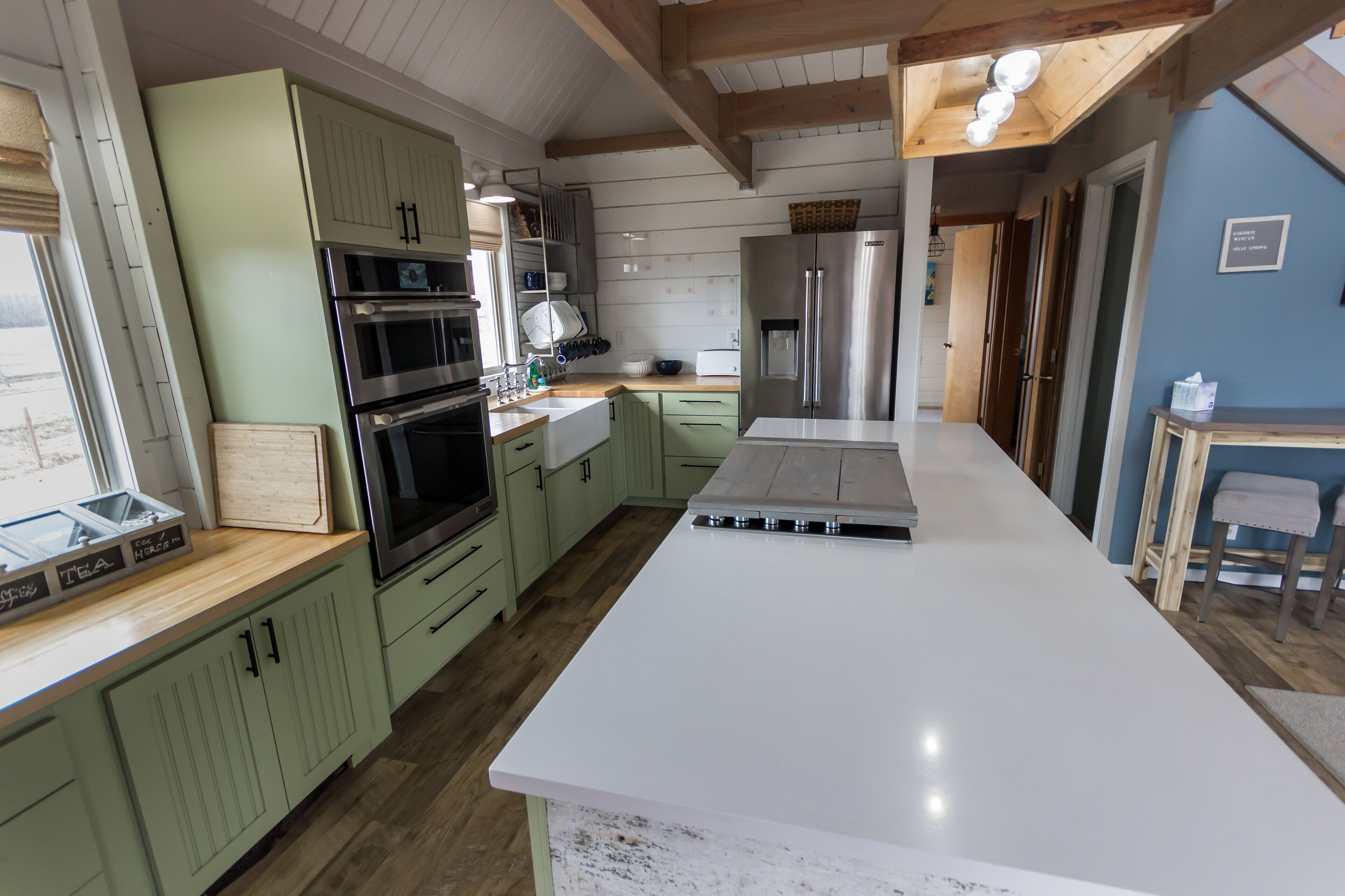 A kitchen with green cabinets, stainless steel appliances, and a white countertop.