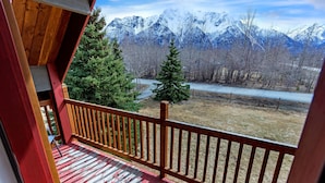 Un pontile in legno con ringhiera rossa che si affaccia su un fiume e montagne innevate.
