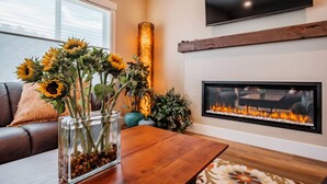 A living room with a fireplace, a TV mounted on the wall, and a vase of sunflowers on a coffee table.