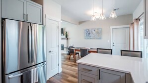 A modern kitchen with stainless steel appliances, a dining area with a table and chairs, and pendant lighting.