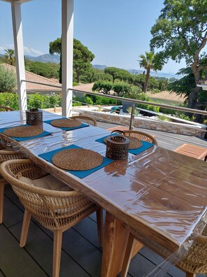 Un espace de restauration en plein air, avec une table en bois et des chaises en osier, aménagé sur une terrasse offrant une vue sur le paysage.