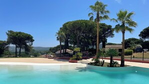 Ein klares, blaues Schwimmbecken, umgeben von Palmen, mit Blick auf eine hügelige Landschaft.