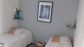 Ein Zimmer mit zwei Betten, einem gerahmten Bild an der Wand, einem kleinen Regal mit einer Vase und einem gemusterten Teppich.